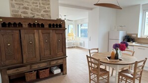A dining area with a wooden table and chairs, a stone wall, and a kitchen in the background.