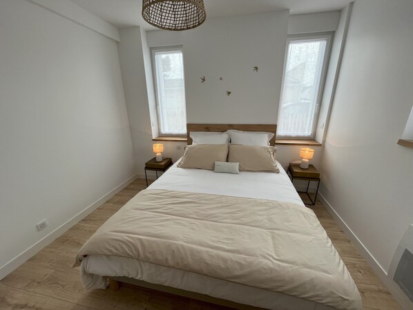 Un dormitorio con una cama grande, dos mesitas de noche con lámparas, un cabecero de madera y una ventana con vistas.