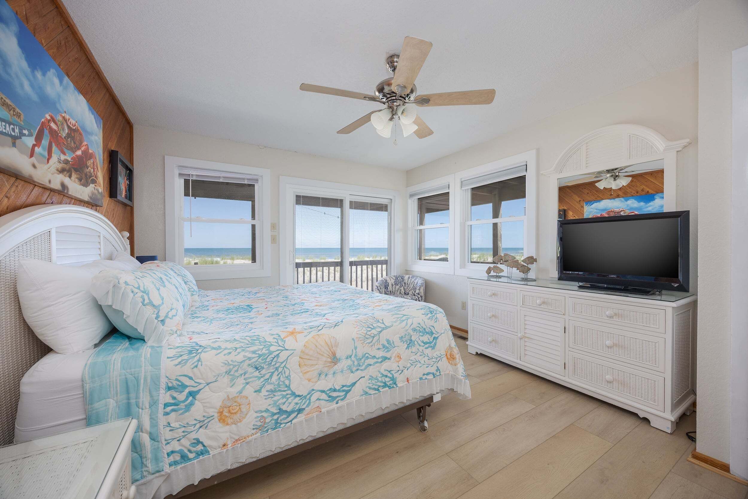 A bedroom with a bed, a television, a ceiling fan, and a view of the ocean.