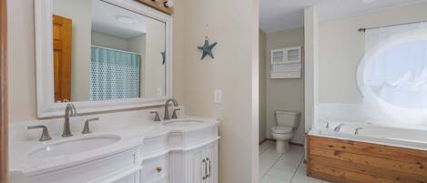 A bathroom with a double sink vanity, a large mirror with lights, a star decoration, and a bathtub.