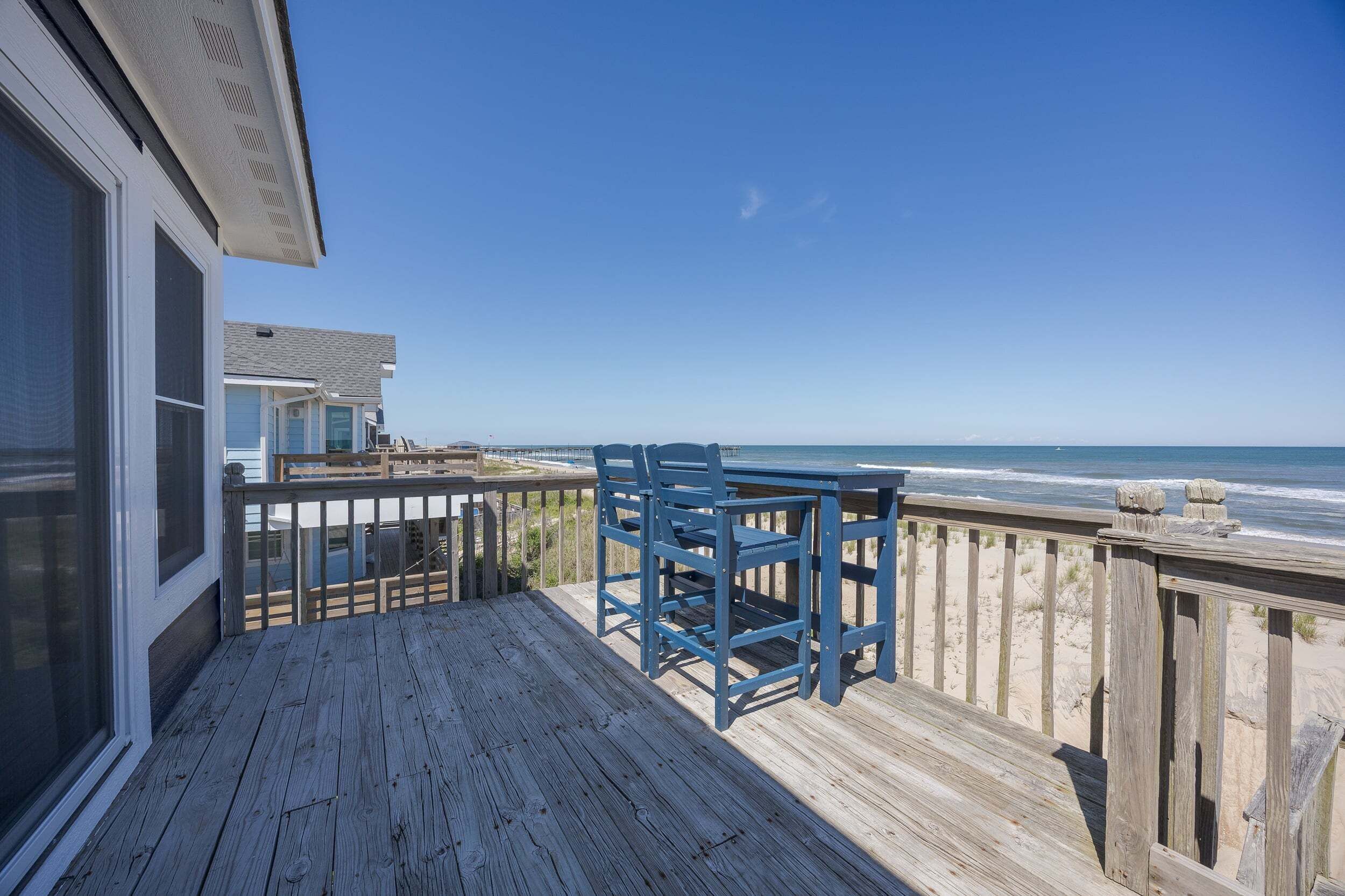 Een houten terras met een tafel en stoelen met uitzicht op een strand.