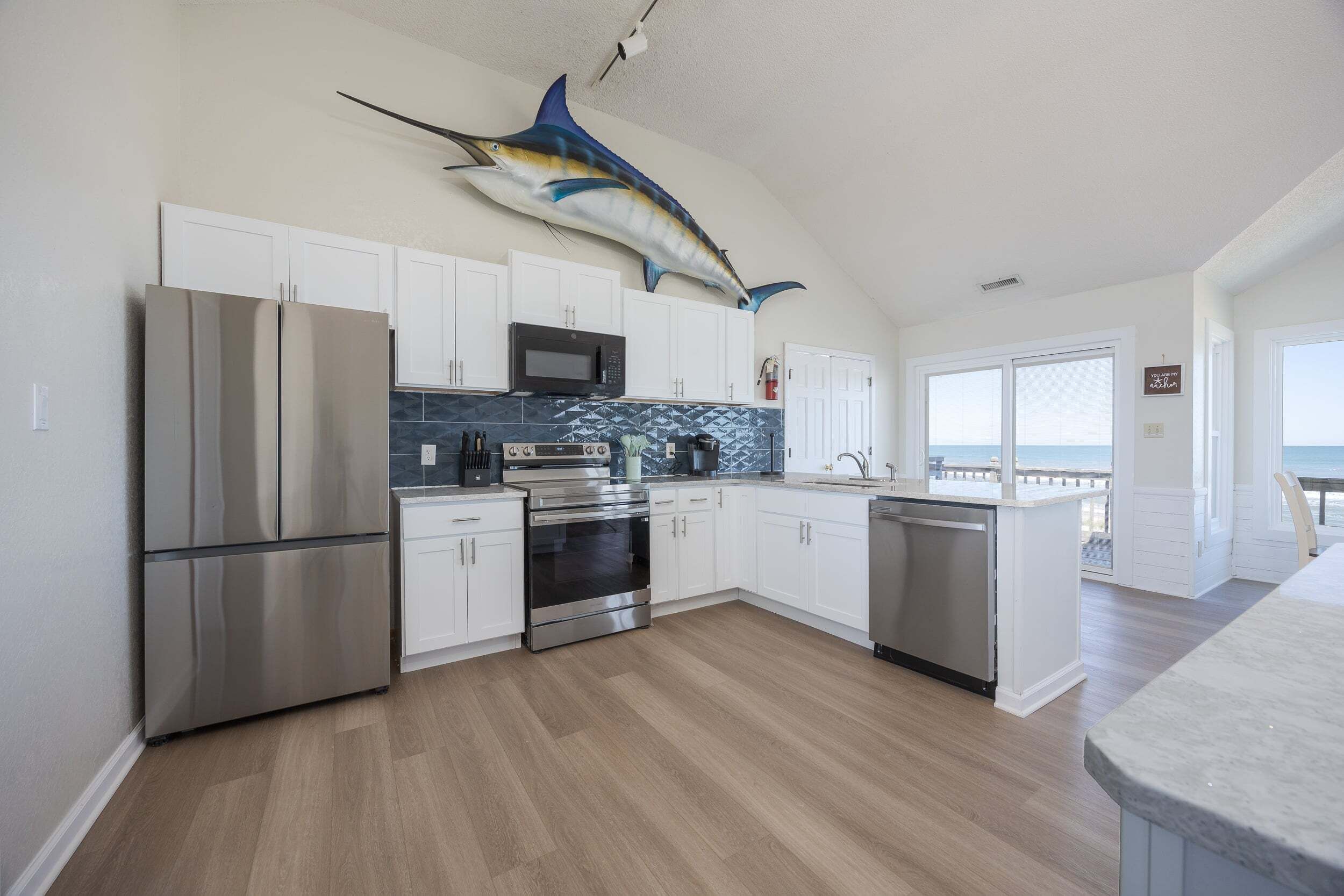 A modern kitchen with white cabinets, stainless steel appliances, a backsplash, and a large fish mural on the ceiling.