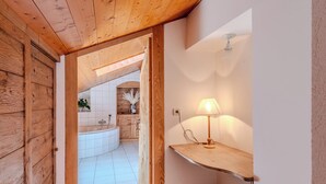 A wooden interior with a bathtub, a lamp on a shelf, and a white tiled floor.
