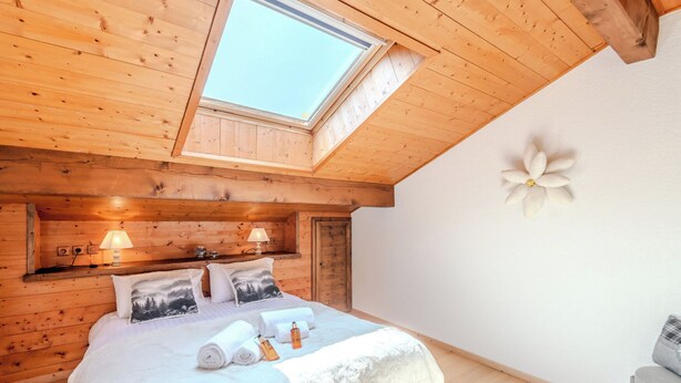 A cozy wooden room with a skylight, a bed with pillows, a nightstand, and a wall decoration.