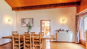 A wooden dining table with chairs, a potted plant, and a radiator in a room with wooden floors and walls.