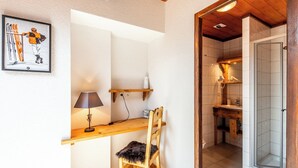 A compact room with a wooden desk, a chair, a lamp, and a framed picture on the wall.