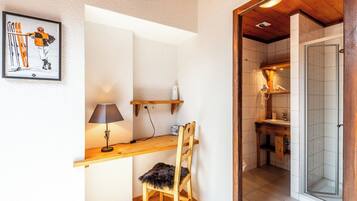 Une pièce de taille modeste, avec un bureau en bois, une chaise, une lampe et un tableau encadré accroché au mur.
