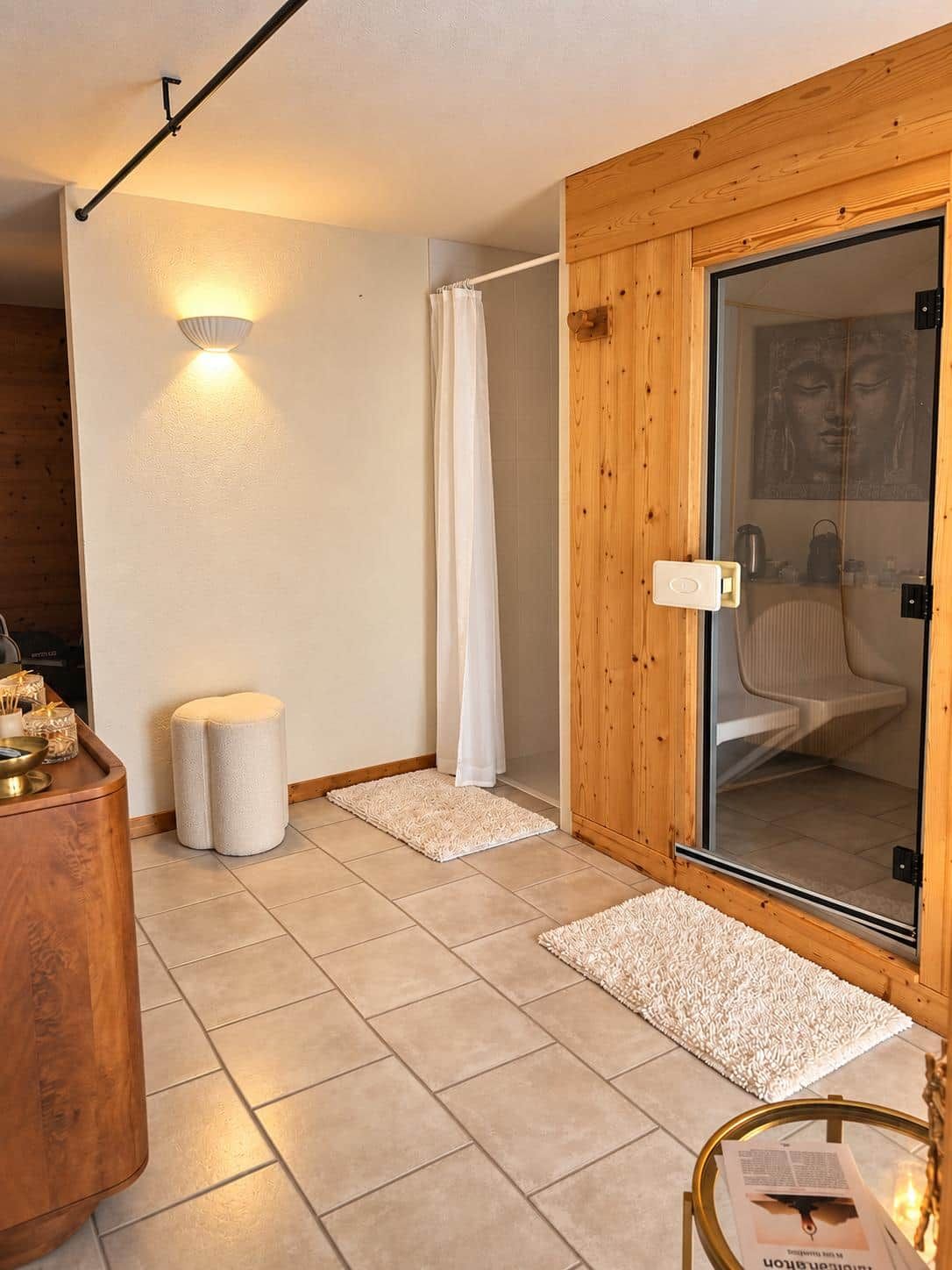 A room with a wooden door, a glass shower enclosure, a white curtain, a small stool, and a table with a bowl and candles.