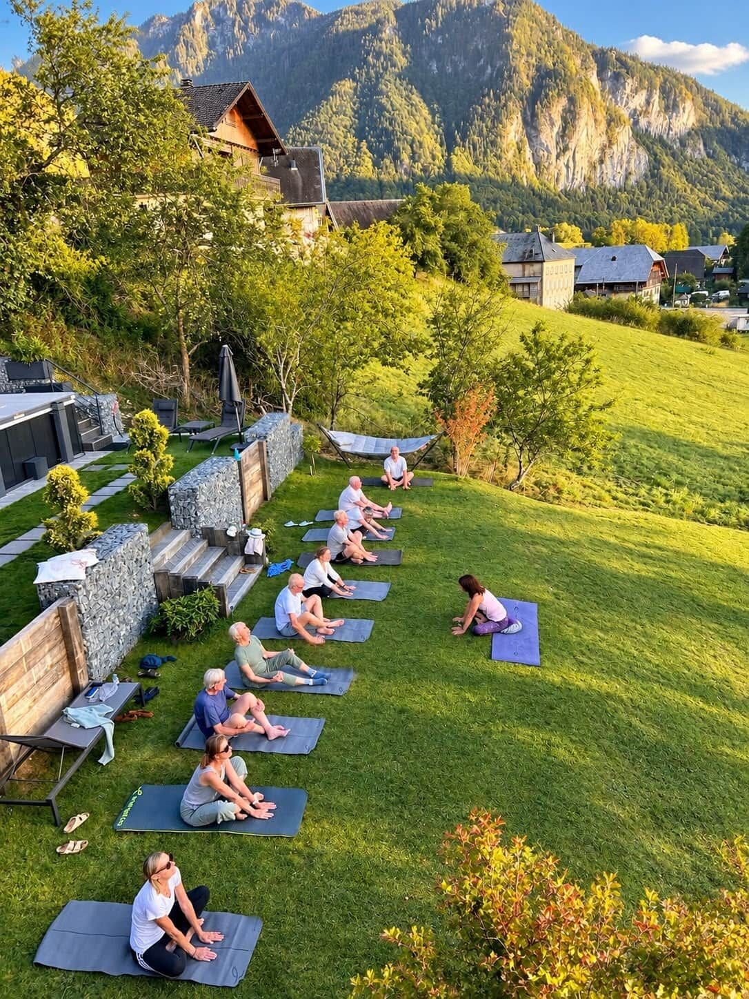 Un groupe de personnes sur des tapis de yoga, en plein air, avec une chaîne de montagnes en arrière-plan.