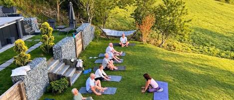 Un groupe de personnes sur des tapis de yoga, en plein air, avec une chaîne de montagnes en arrière-plan.