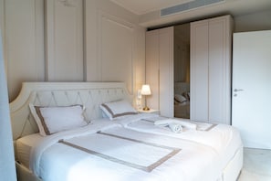 Ein ordentlich bezogenes Bett mit Kopfteil, einer Nachttischlampe und einem Schrank mit Spiegel.