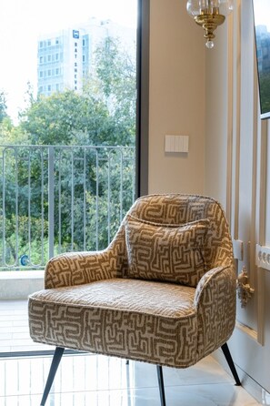 Ein moderner Sessel mit geometrischem Muster, platziert in der Nähe eines Fensters mit Blick auf einen Balkon und die Stadtlandschaft.