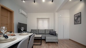 Un salon moderne avec un canapé gris, une table à manger avec des chaises et une fenêtre avec des stores.
