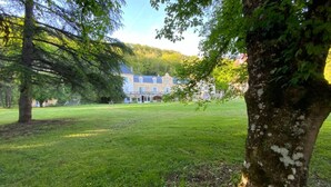Un edifici gran i antic amb façana simètrica i nombroses finestres, envoltat d'un jardí ben cuidat i arbres.