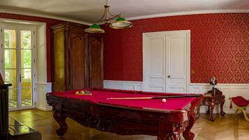 Een biljarttafel in een kamer met rood behang, houten kasten en een deur.