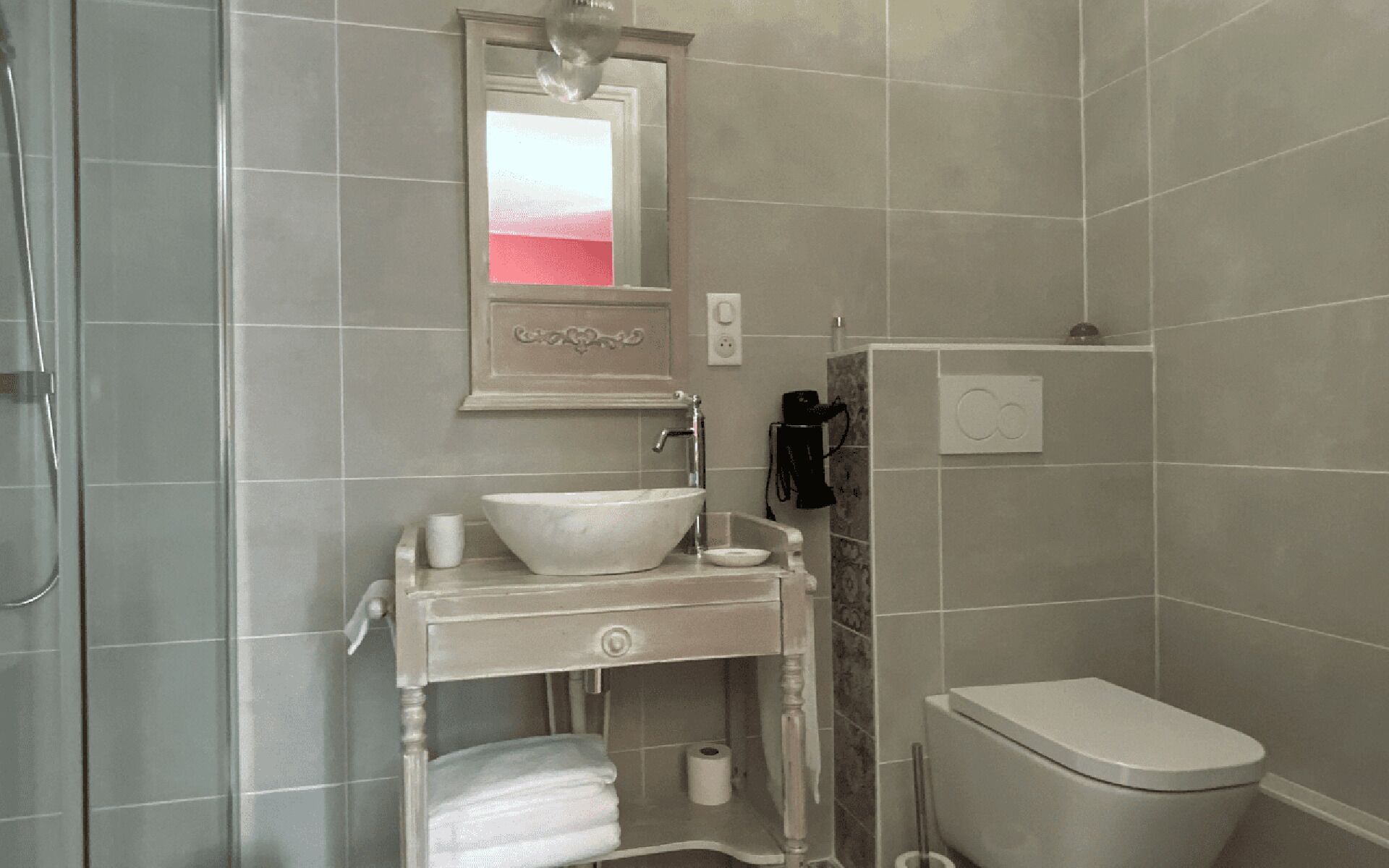 Een badkamer met een wit wastafel, een spiegel, een toilet en een douchegedeelte.