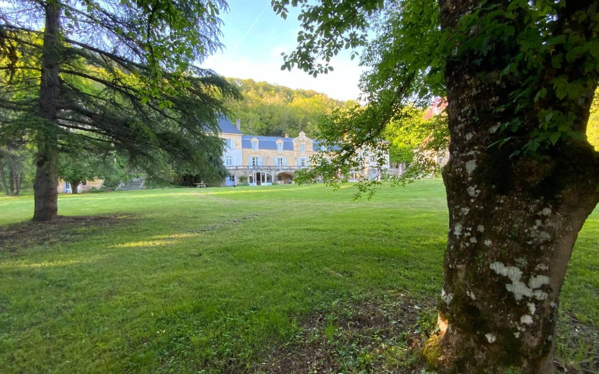 A large, historic building with a symmetrical facade and multiple windows, surrounded by a well-maintained lawn and trees.