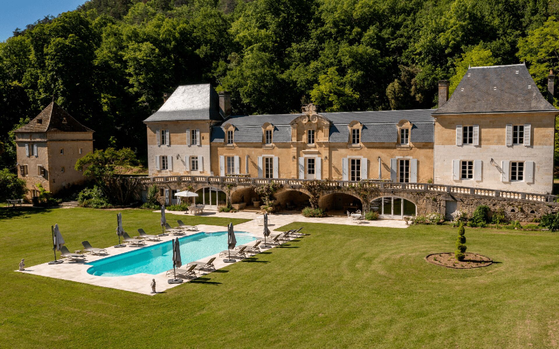 A large estate with a swimming pool, outdoor seating, and a stone bridge.