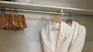 A white robe hanging on a metal rod in a closet with a wooden hanger rack to the left. - Spacious Design Loft/Railyard Distr; soaking tub (Santa Fe)