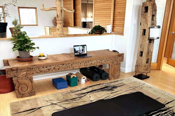 Un banc en bois orné de sculptures complexes, un ordinateur portable et une plante en pot, dans une pièce moderne aux murs en bois et dotée d’un grand miroir.