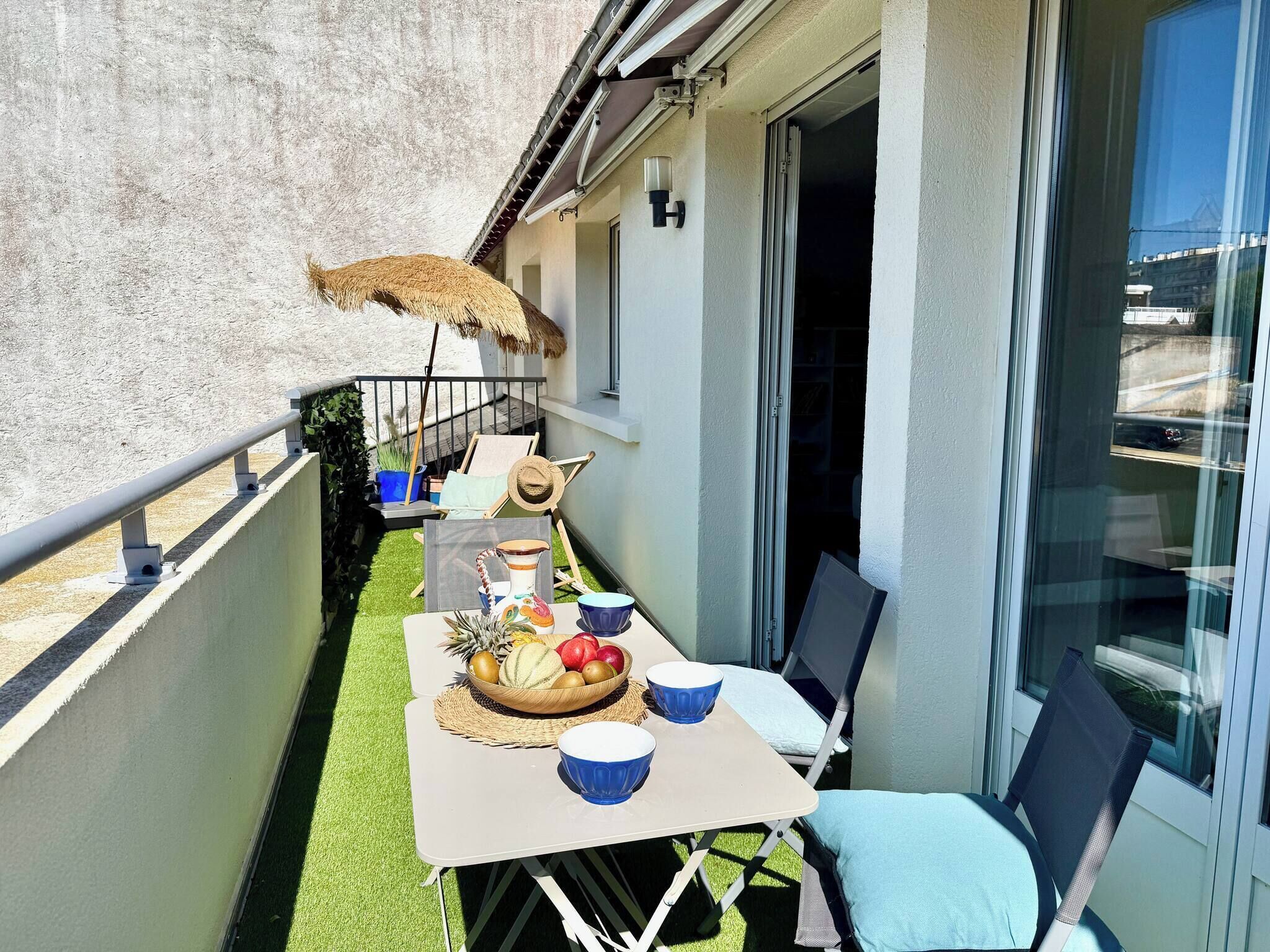 A balcony with a table set for dining, a chair, a thatched umbrella, and a window.