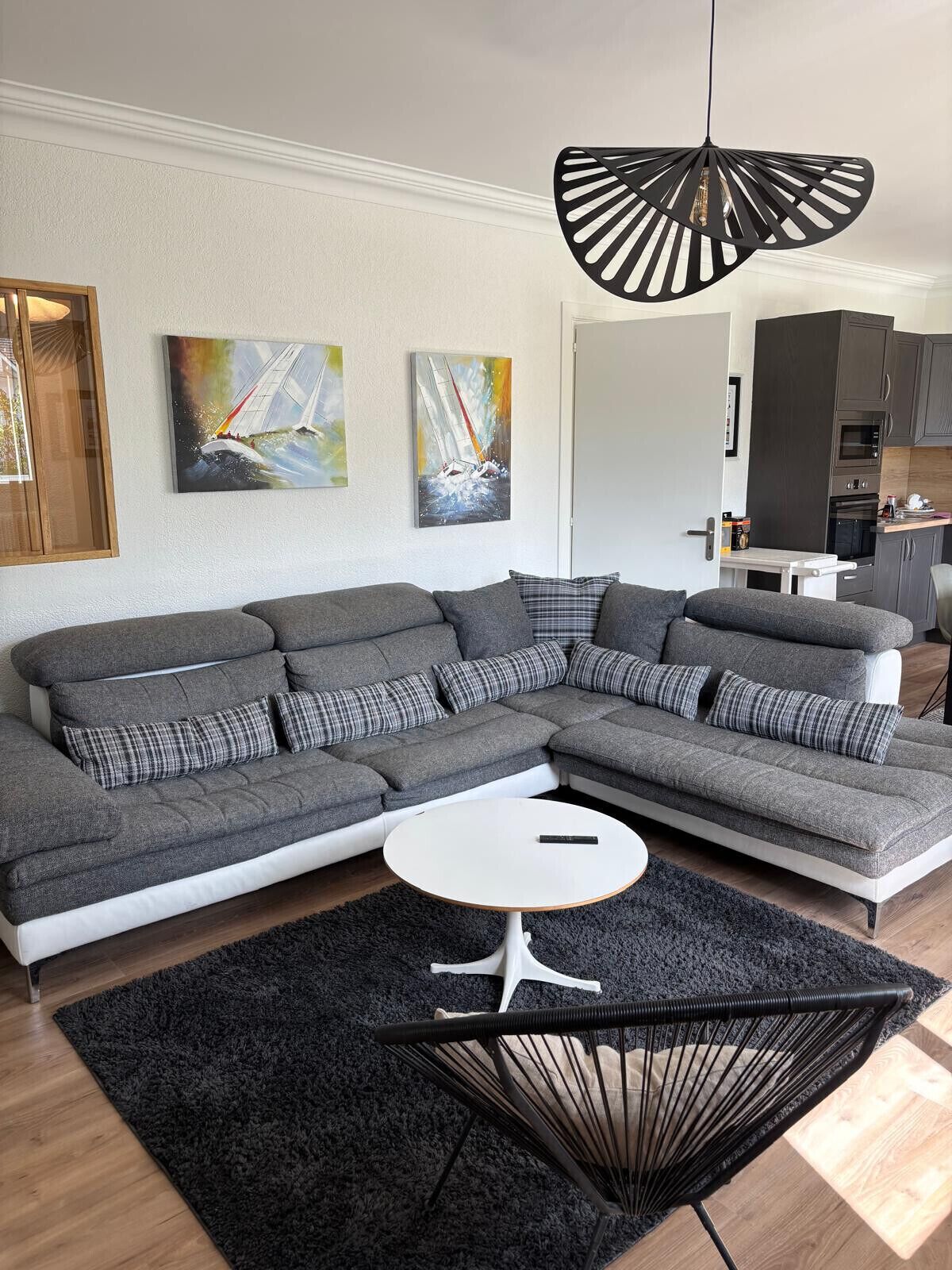 A modern living room with a sectional sofa, a round coffee table, a black woven chair, and artwork on the walls.