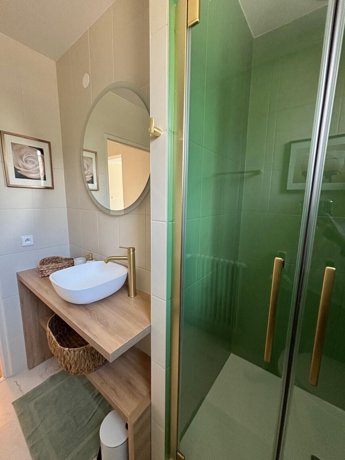 Un baño con un lavabo blanco, un espejo redondo y una zona de ducha con azulejos verdes.
