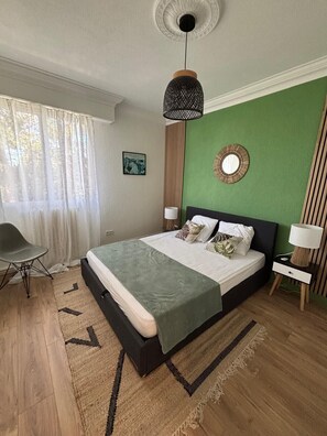 A bedroom with a bed, a chair, a lamp, a wall clock, and a ceiling light fixture. - Les Platanes : La baule (La Baule-Escoublac)