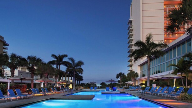 Ein Swimmingpool mit Liegestühlen und Palmen, umgeben von Hotelgebäuden.