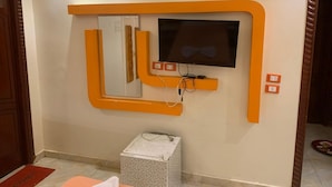 Una habitación con televisión montada en la pared, con un marco naranja, una mesita y una silla.