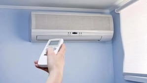 Una mano sostiene un control remoto cerca de un aire acondicionado instalado en la pared.