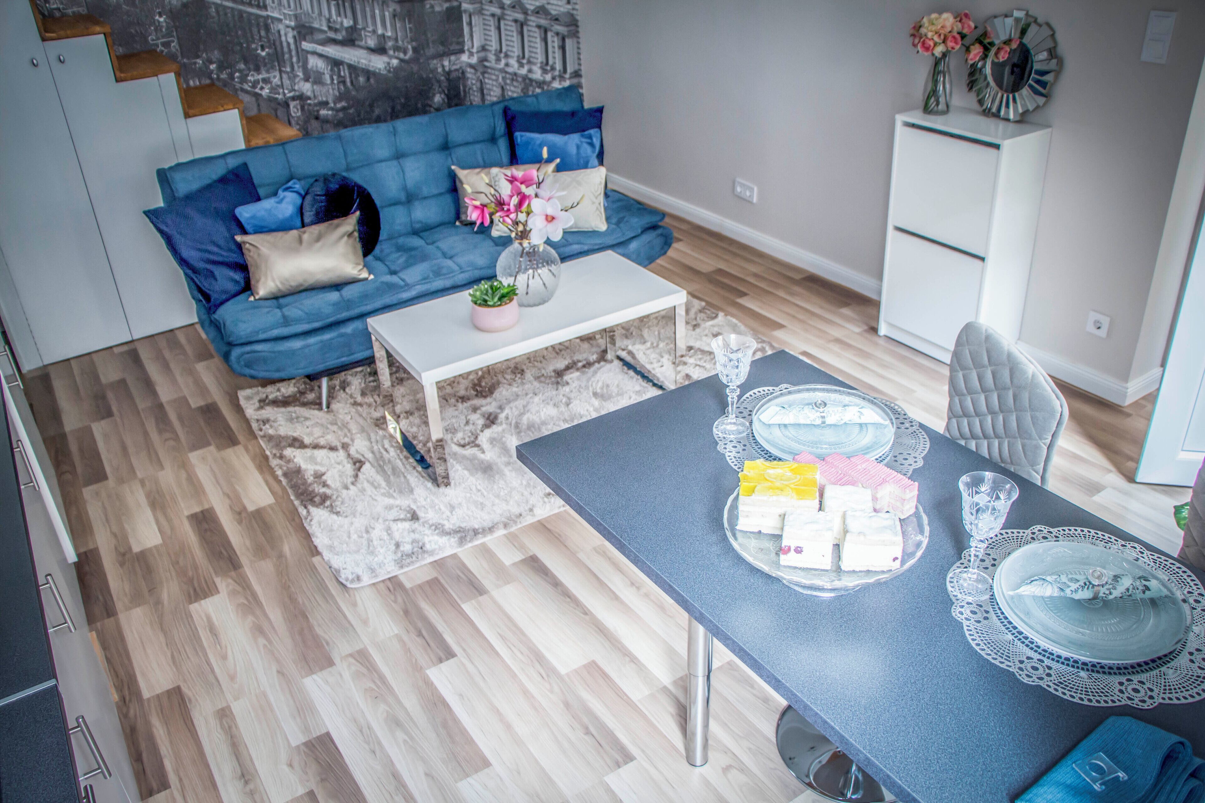 Un salon moderne avec un canapé bleu, une table basse blanche et un coin repas avec une table dressée pour quatre personnes.