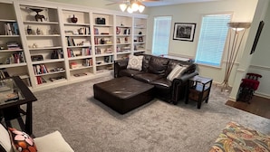 A living room with a sectional sofa, a coffee table, a bookshelf, a ceiling fan, and a patterned rug.