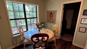 A dining area with a round table, chairs, a ceiling fan, and a window with a view of trees.