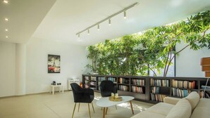 A modern living room with a sofa, two chairs, a coffee table, a bookshelf, and a large green plant wall.