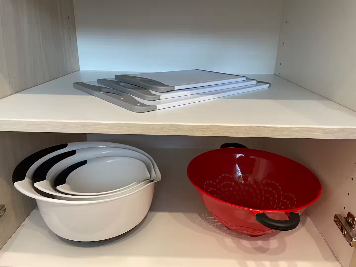 A kitchen shelf with white bowls, a red colander, and a stack of white plates.