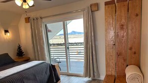 Un dormitorio con una cama, un banco de madera, un pequeño árbol de Navidad y vistas a un paisaje montañoso a través de un ventanal corredero.