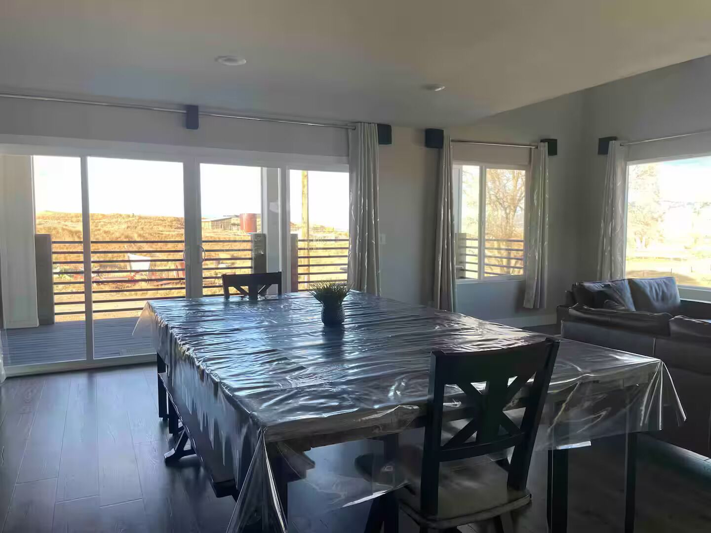 Une pièce spacieuse avec une grande table recouverte de plastique, un canapé et une vue sur un espace extérieur clôturé.