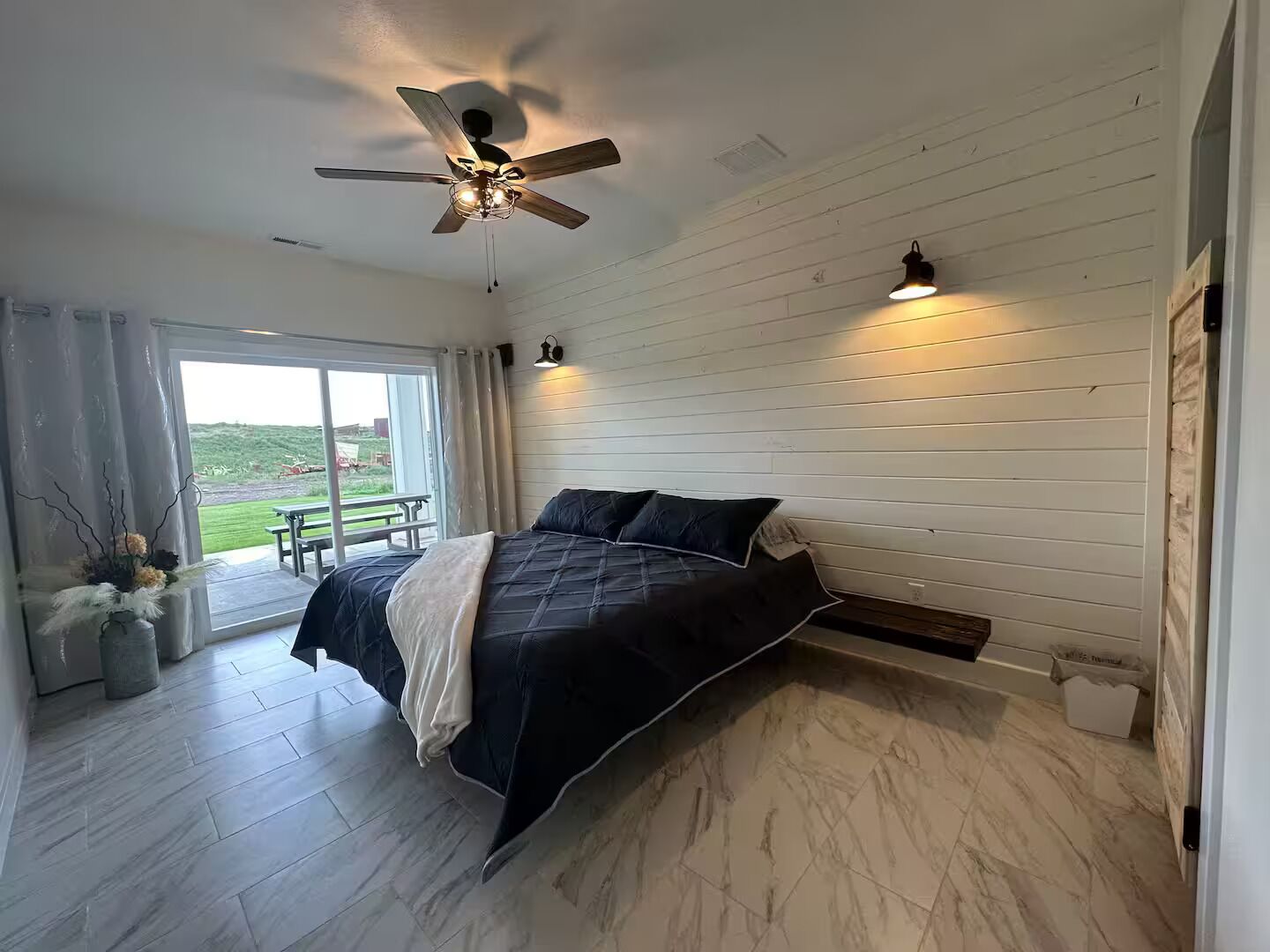 Une chambre à coucher avec un lit, un ventilateur de plafond, une fenêtre et une vue sur l’extérieur.