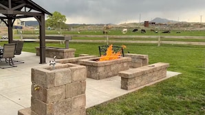 Un patio exterior con un hogar para fuego, asientos y vistas a un campo con vacas.