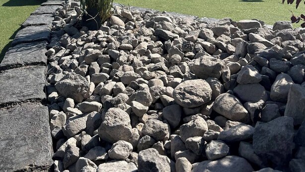 Un campo de golf con un césped de práctica bien cuidado, rodeado por un borde de piedra y rocas dispersas.