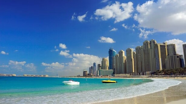 A beach with clear turquoise water, a sandy shore, and a city skyline in the background.