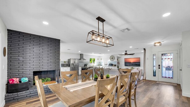A modern kitchen with a stone backsplash, wooden dining table, and chairs.