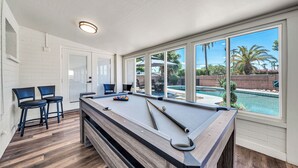 A pool table with a clear view of a swimming pool outside.