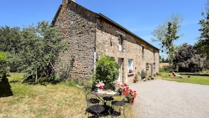 Un bâtiment en pierre avec une allée en gravier et une table ronde entourée de chaises devant.