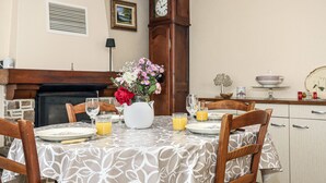 Un coin repas avec une table dressée pour quatre personnes, un vase de fleurs et une horloge au mur.