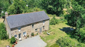 Une maison en pierre avec un toit en pente, entourée d’une végétation luxuriante et sous un ciel dégagé.