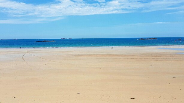 Une vaste plage de sable fin, sous un ciel bleu dégagé et une mer calme.