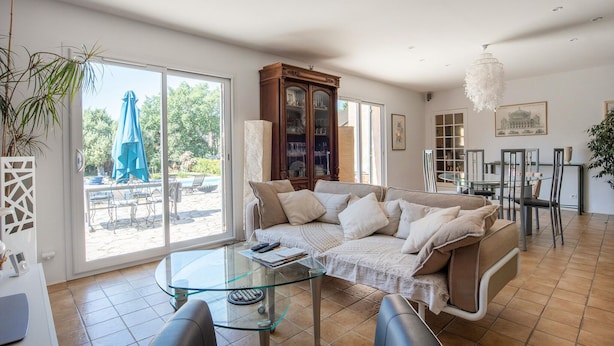 A spacious living room with a glass coffee table, a sofa with cushions, a dining area with chairs, and a view of the outdoor patio. - Lovely home in Saint Cezaire (Saint Cezaire)