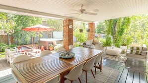A covered patio with a wooden table and chairs, a red umbrella, and a brick pillar.